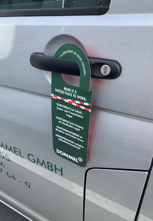 Hinweisschild am Autotürgriff: Empfehlungen für Arbeitssicherheit mit Schutzbrille und Schutzvorrichtungen.