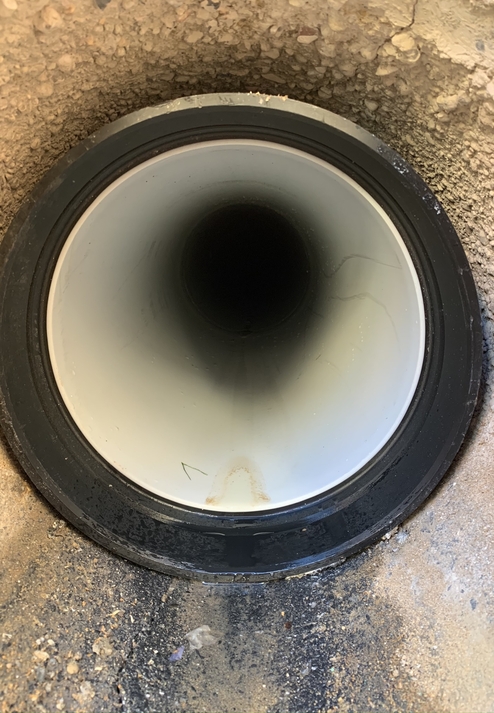 Blick auf das Innere eines großen Rohrleders mit schwarzem Rand, umgeben von grobem, schmutzigem Untergrund.