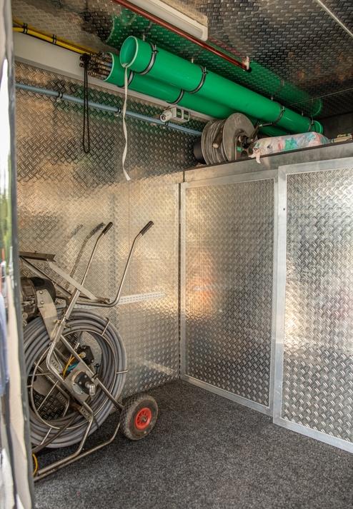 Innenraum eines Fahrzeugs mit metallischen Wänden, grauen Schläuchen und einem Werkzeugwagen auf einem Teppichboden.