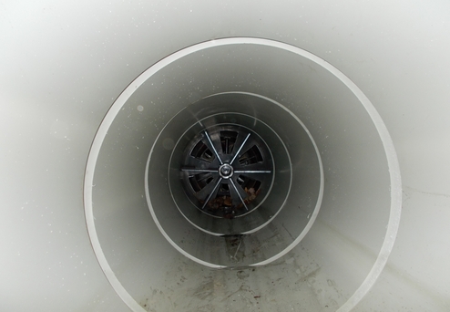 Blick in ein spiralförmiges Rohr mit einem Metallgitter und Ablagerungen am Boden.