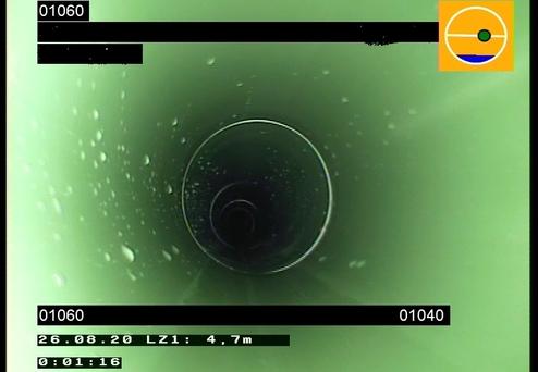 Blick in ein langes, grünes Rohr mit Wasserbläschen vor einem dunklen Hintergrund.