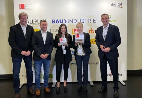 Fünf Personen stehen vor einer Wand mit Sponsorenlogos und halten Preise des Deutschen Baupreises 2022 in der Hand.