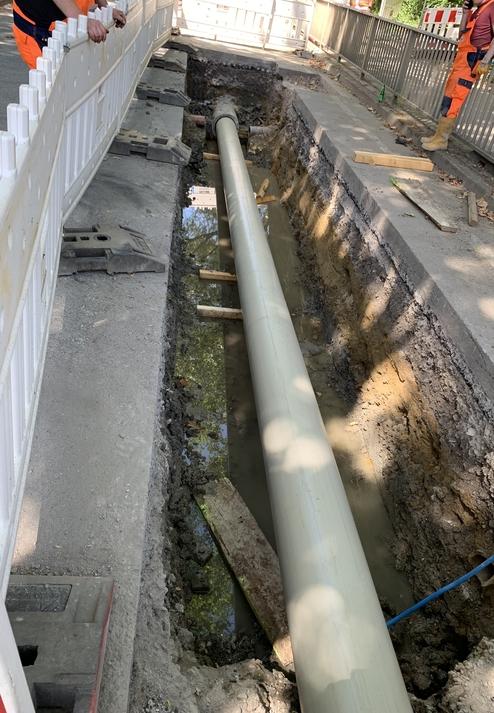 Baugrube mit einem langen Rohr, das in der Mitte verlegt ist, umgeben von Erdreich und Wasseransammlungen.