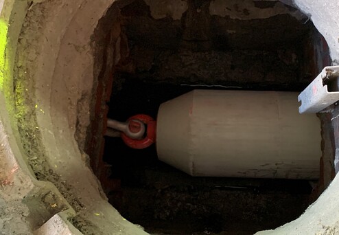 Ansicht eines tiefen Schachts mit einem weißen Zylinder und einem roten Verbindungselement in einem dunklen Raum.