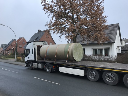 Lkw mit einer großen, zylindrischen Last auf der Ladefläche fährt an Wohnhäusern vorbei.